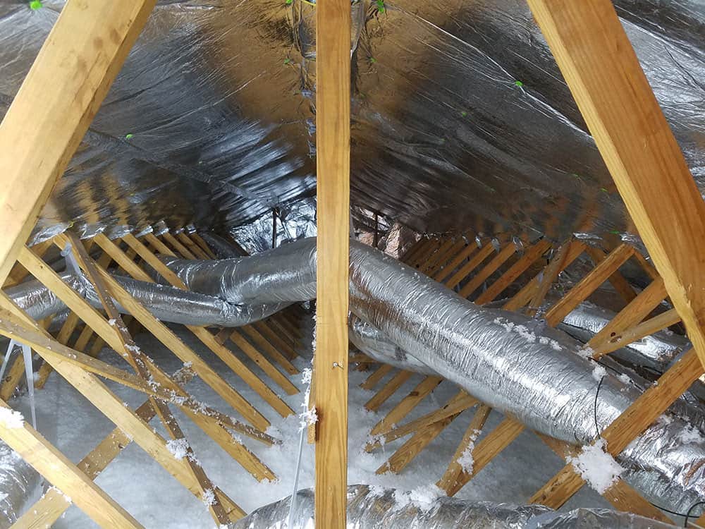Installer fitting a reflective radiant barrier panel against roof sheathing