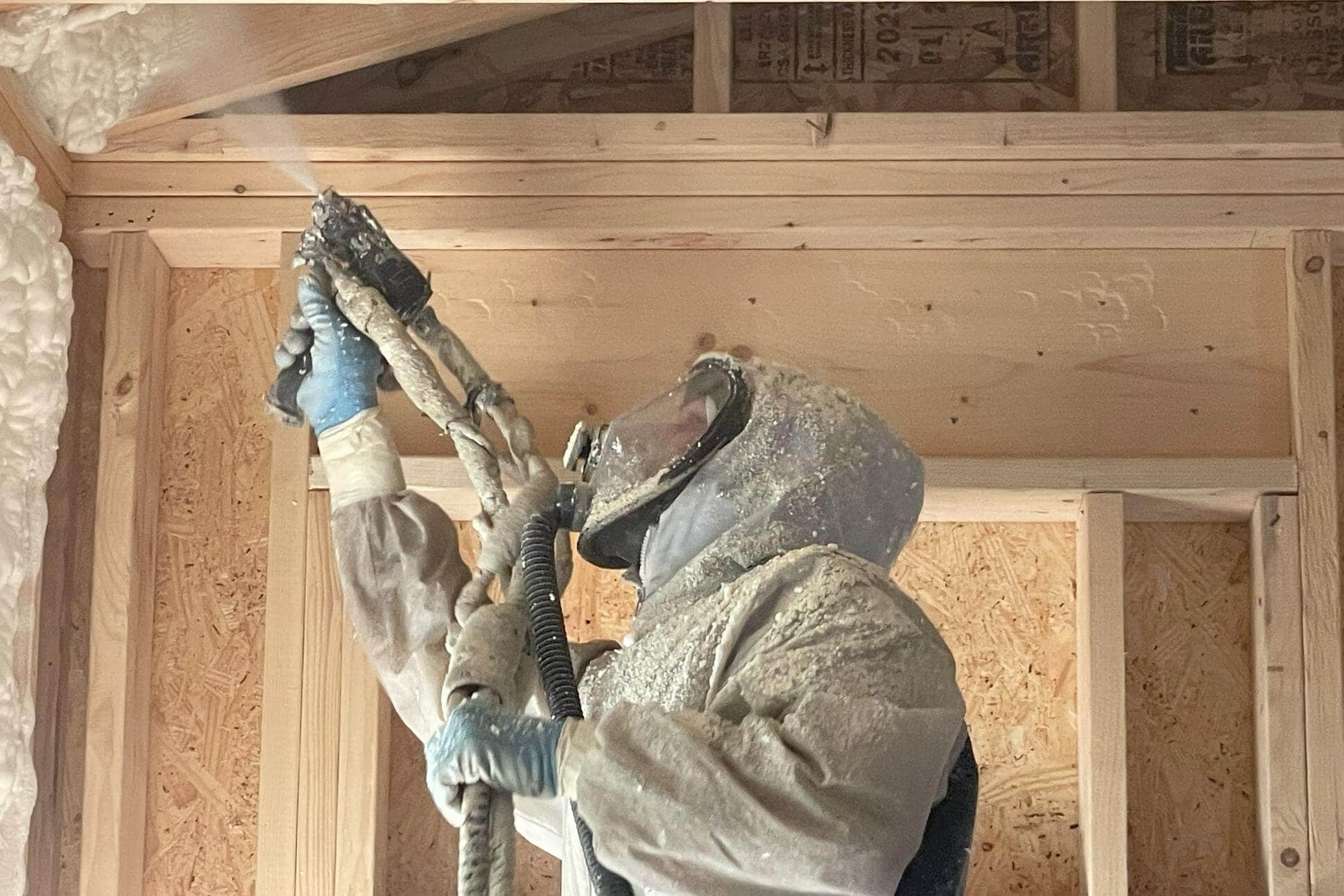 VR Insulation technician spraying polyurethane foam into a stud wall cavity